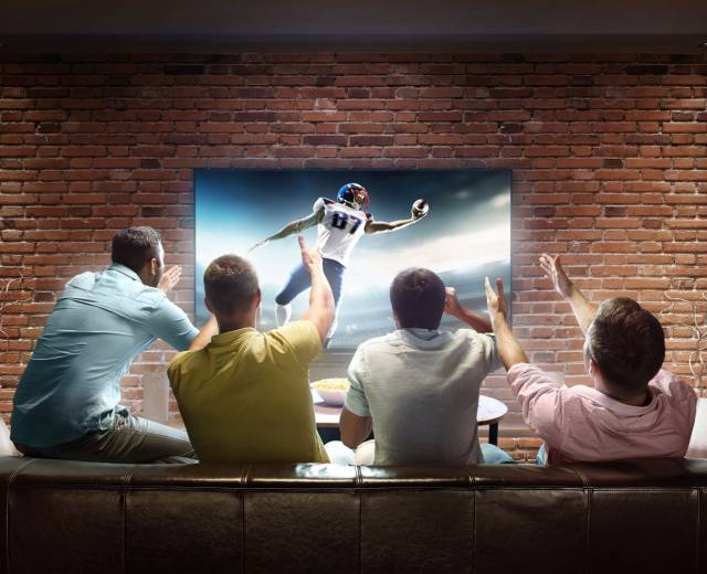 four men sit on a couch watching football in Lincoln City, OR