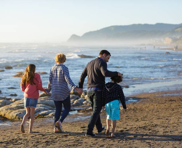 A family of four walk on the beach along the Oregon coast as waves roll in to their left.