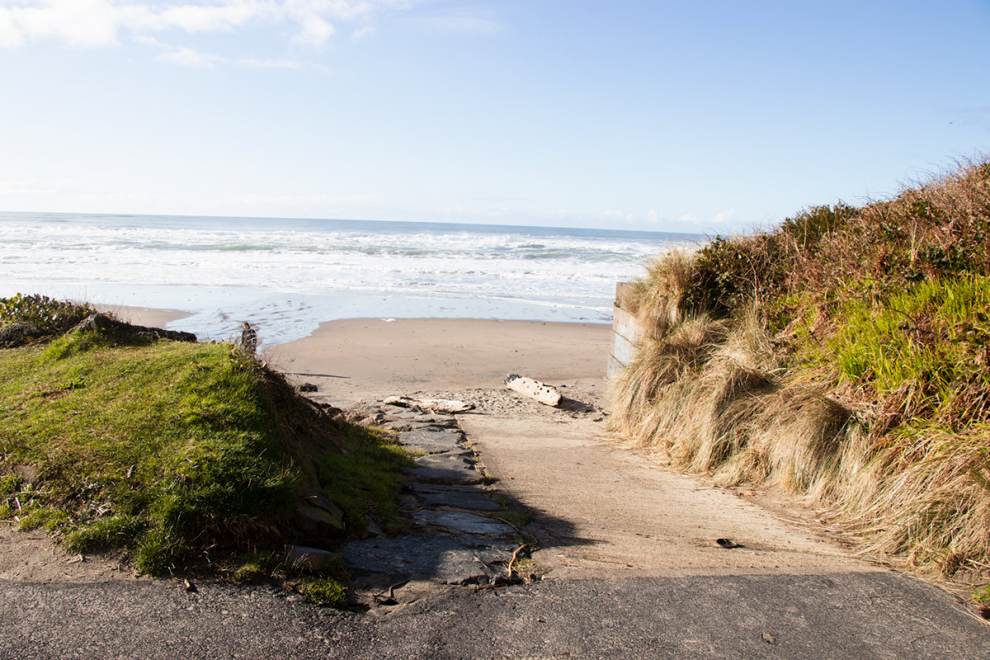 a handicap accessible path cuts through plant-covered dunes leading to a sandy beach and ocean waves