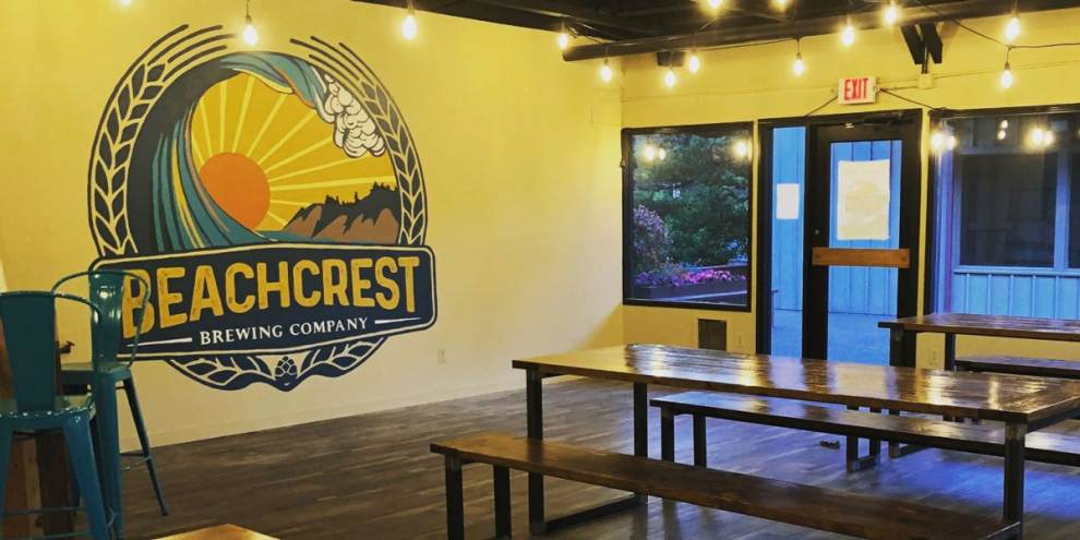 interior of Beachcrest Brewing Company featuring a mural of the company logo, yellow walls, and long tables at Oregon Coast