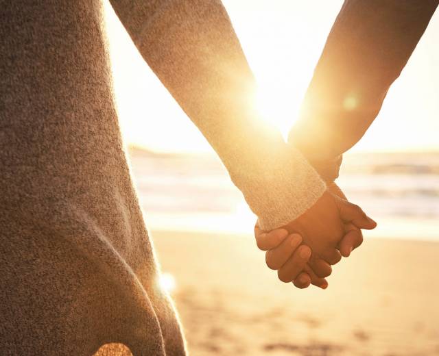 Close-up of a couple holding hands at sunset on the beach