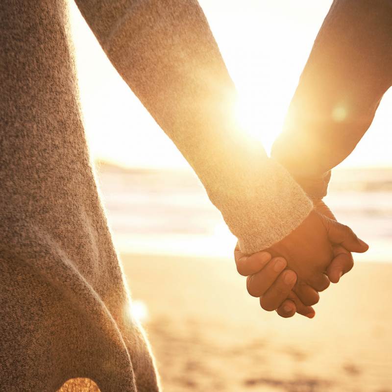 Close-up of a couple holding hands at sunset on the beach