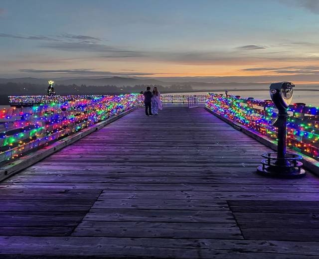 a couple admires the colorful Christmas lights decorating Taft Dock at sunset in Lincoln City, OR