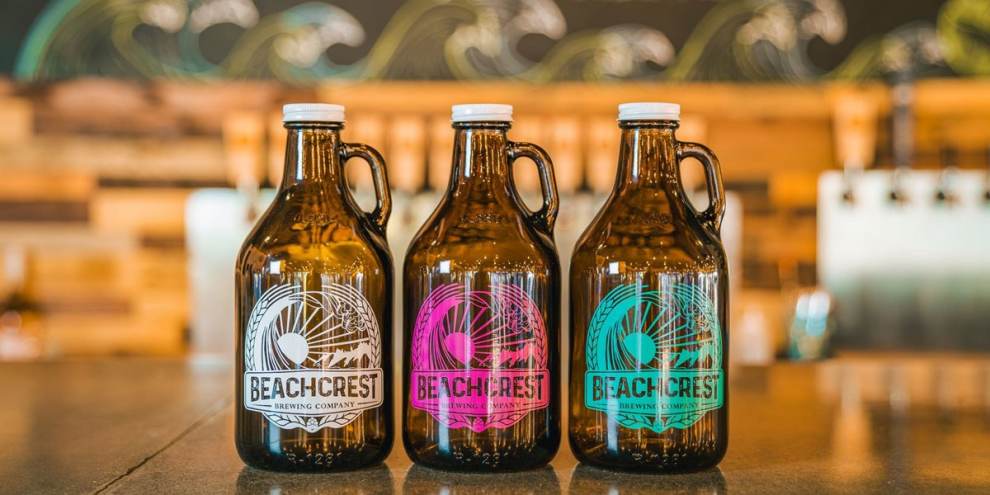 three amber bottles on a counter each with a different color Beachcrest logo, one white, one pink and one teal