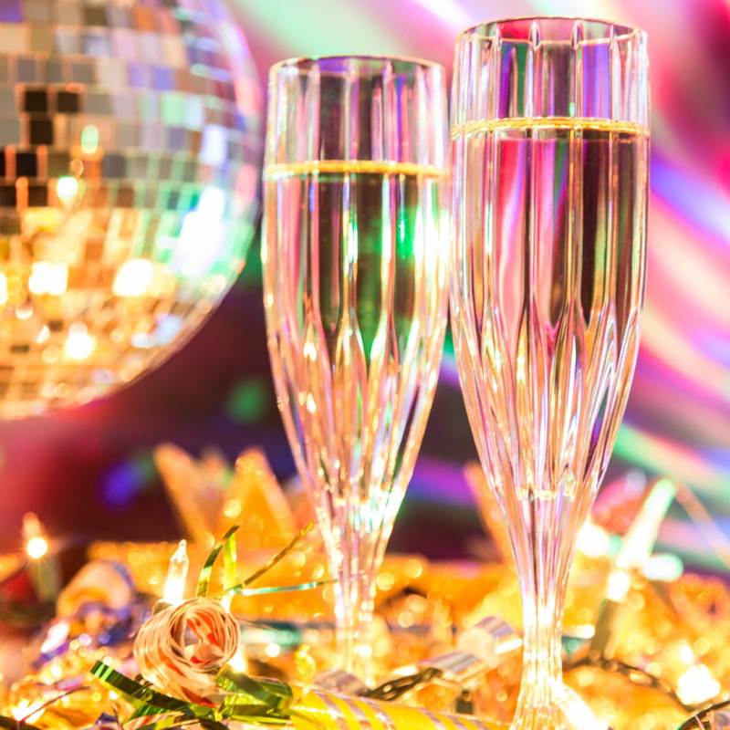 two flutes of champagne and a bottle on a table in front of a disco ball and colorful lights