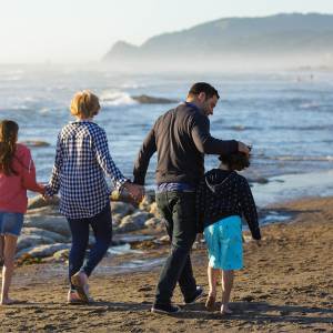 Family of four holds hands while walking on the beach in Lincoln City, OR