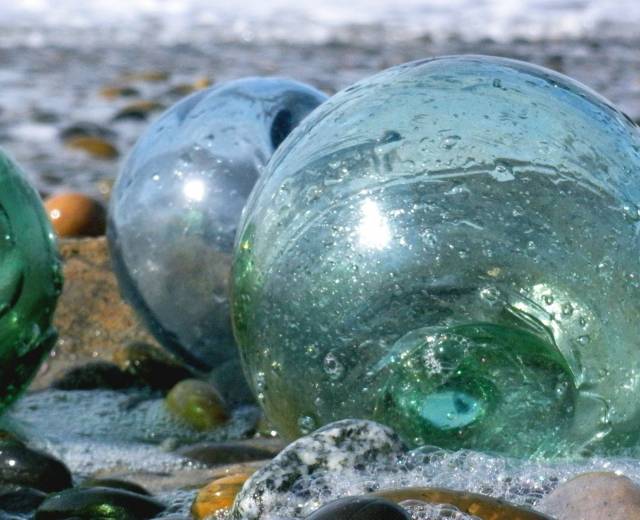 close-up of two green and two blue glass floats on the beach in lincoln city