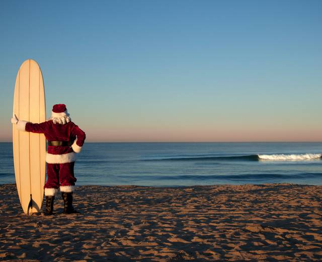 santa with a surfboard on the beach looking out at the ocean