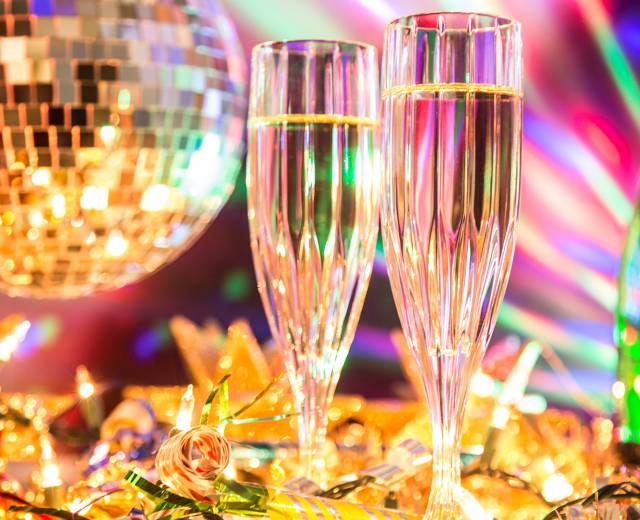 two champagne glasses filled with champagne sit on a table in front of a disco ball and colorful lights on New Years Eve