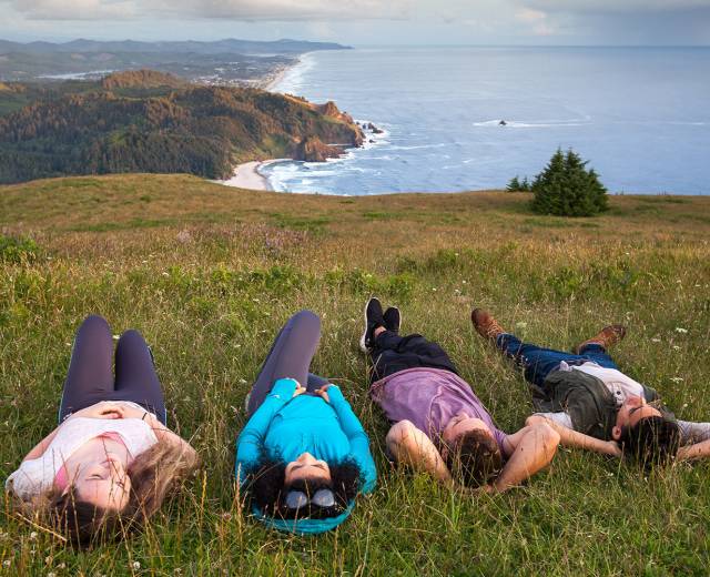 Group of friends laying a grassy cliff overlooking water in Lincoln City, OR