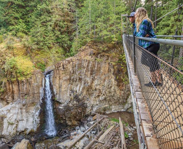 two people look out over a waterfall from a pedestrian bridge while hiking near Lincoln City