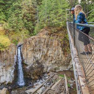 two people look out over a waterfall from a pedestrian bridge while hiking near Lincoln City