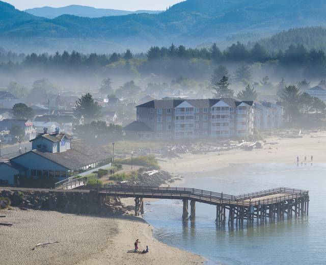 people enjoy the beach at the Taft District in Lincoln City, OR as fog rises between buildings in the distance